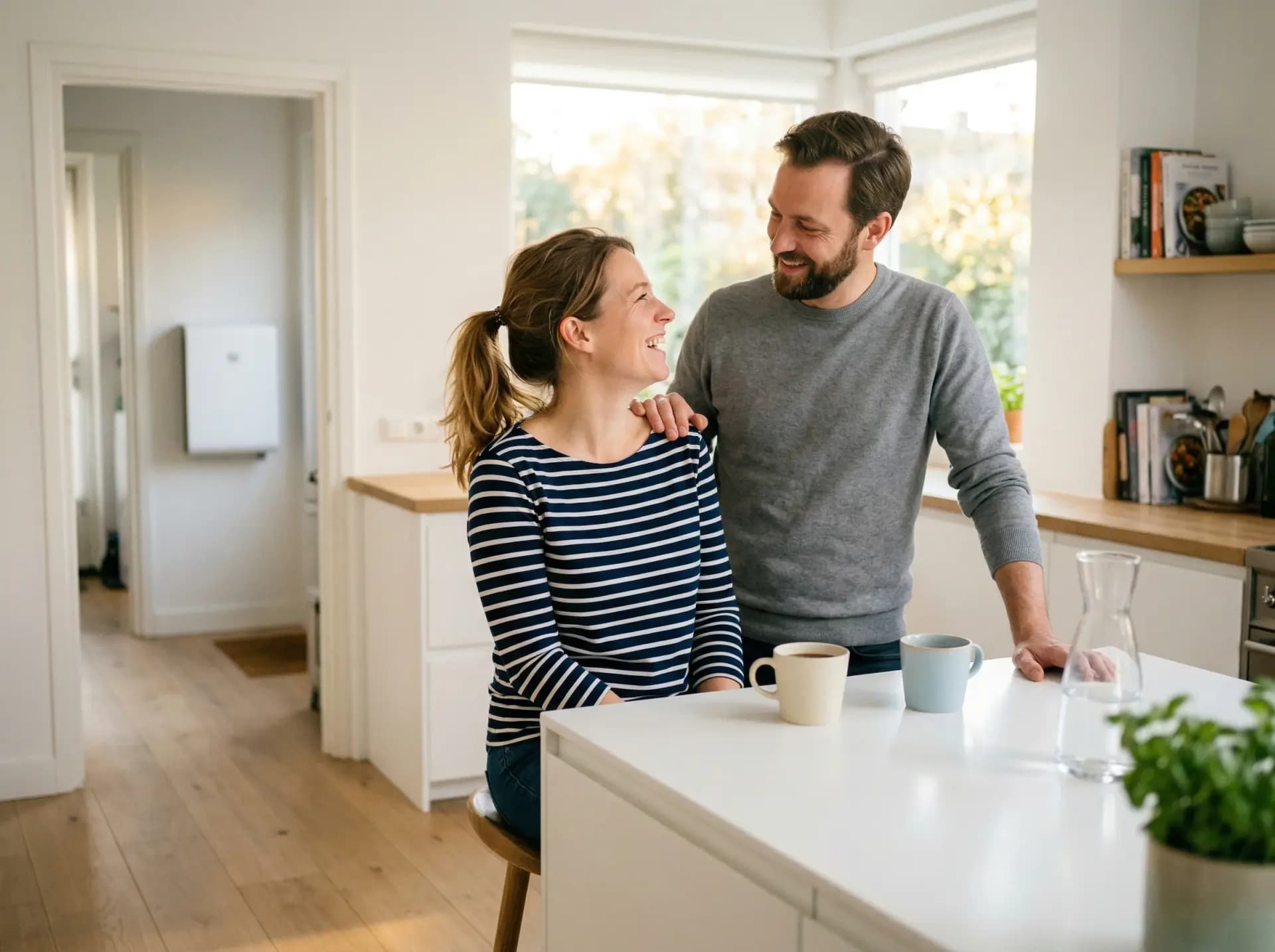 Lachend stel in moderne Nederlandse keuken met thuisbatterij zichtbaar in hal