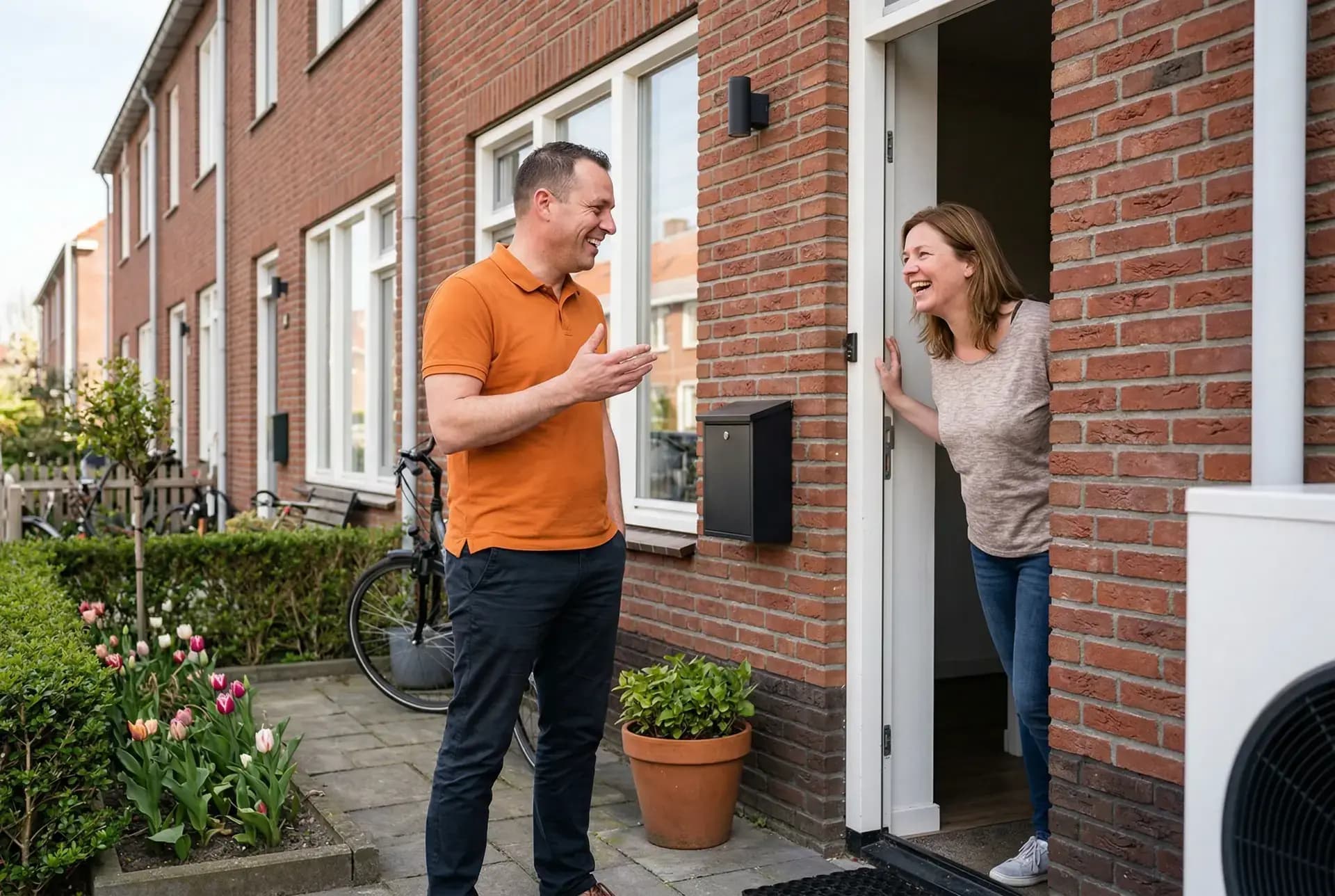 Anteas energieadviseur in oranje polo lacht met huiseigenaar bij voordeur van rijtjeswoning