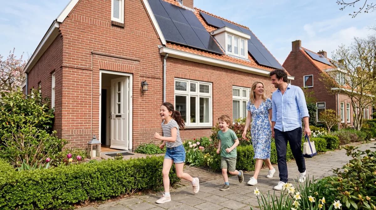 Gezin arriveert thuis en loopt door de voortuin terwijl zonnepanelen op het dak zichtbaar zijn