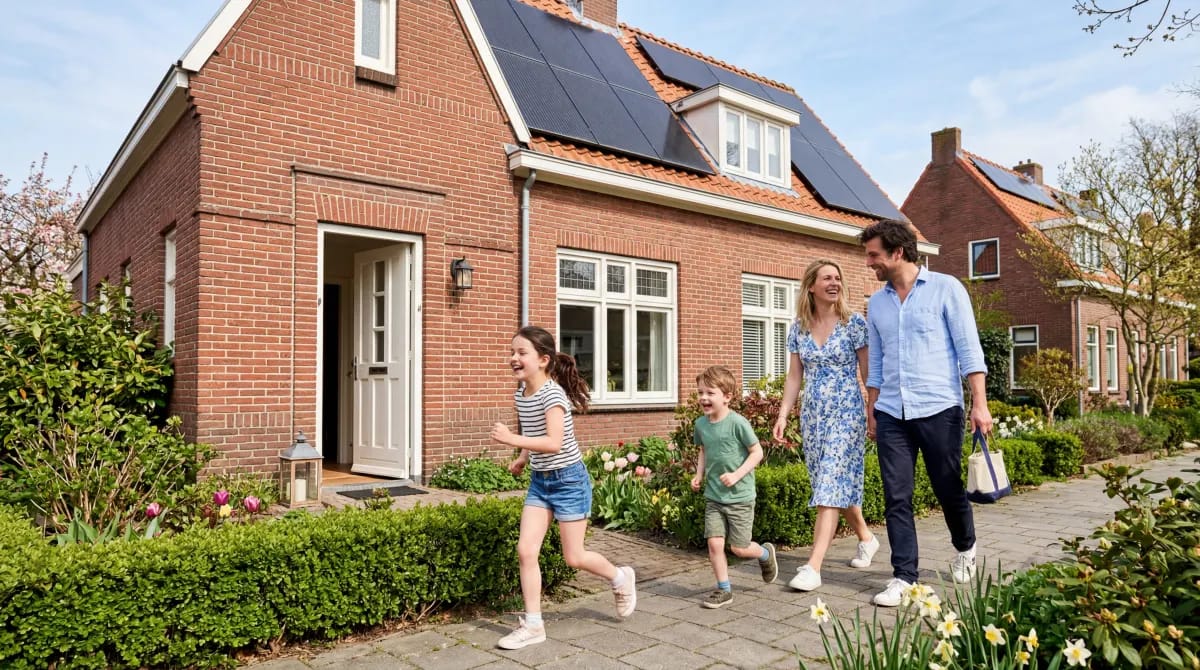 Gezin arriveert thuis en loopt door de voortuin terwijl zonnepanelen op het dak zichtbaar zijn